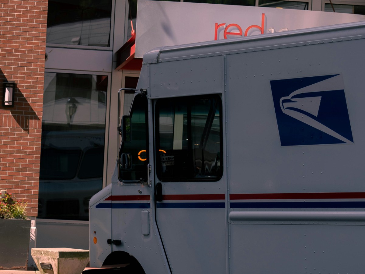 A marine logistics shipmaster in San Diego auditing a batch of maritime manifest logs and applying forever stamps bought with a credit card online with a cargo ship in the background.