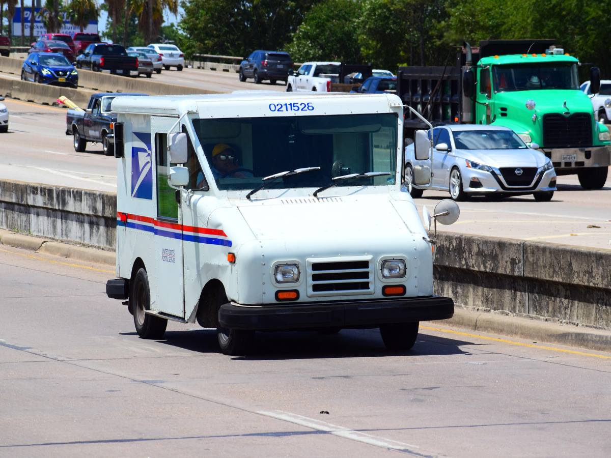 A SLC gov agency administrator in his office auditing a batch of regulatory packets and applying stamps from a usps self-service kiosk with the city skyline in the background.