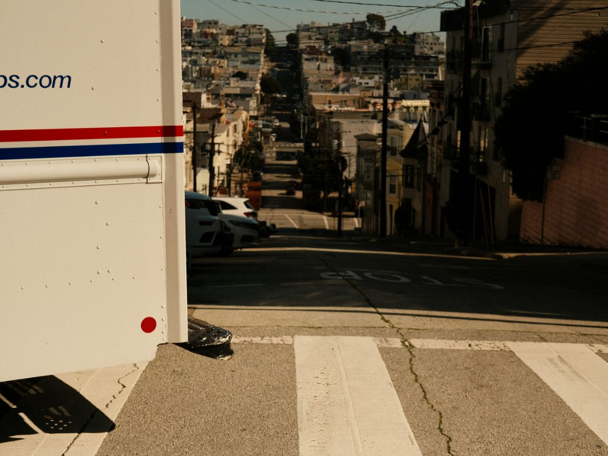 A Manhattan law partner in his office auditing a batch of litigation discovery bundles and applying discount postage stamps from a professional coil with the city skyline in the background.